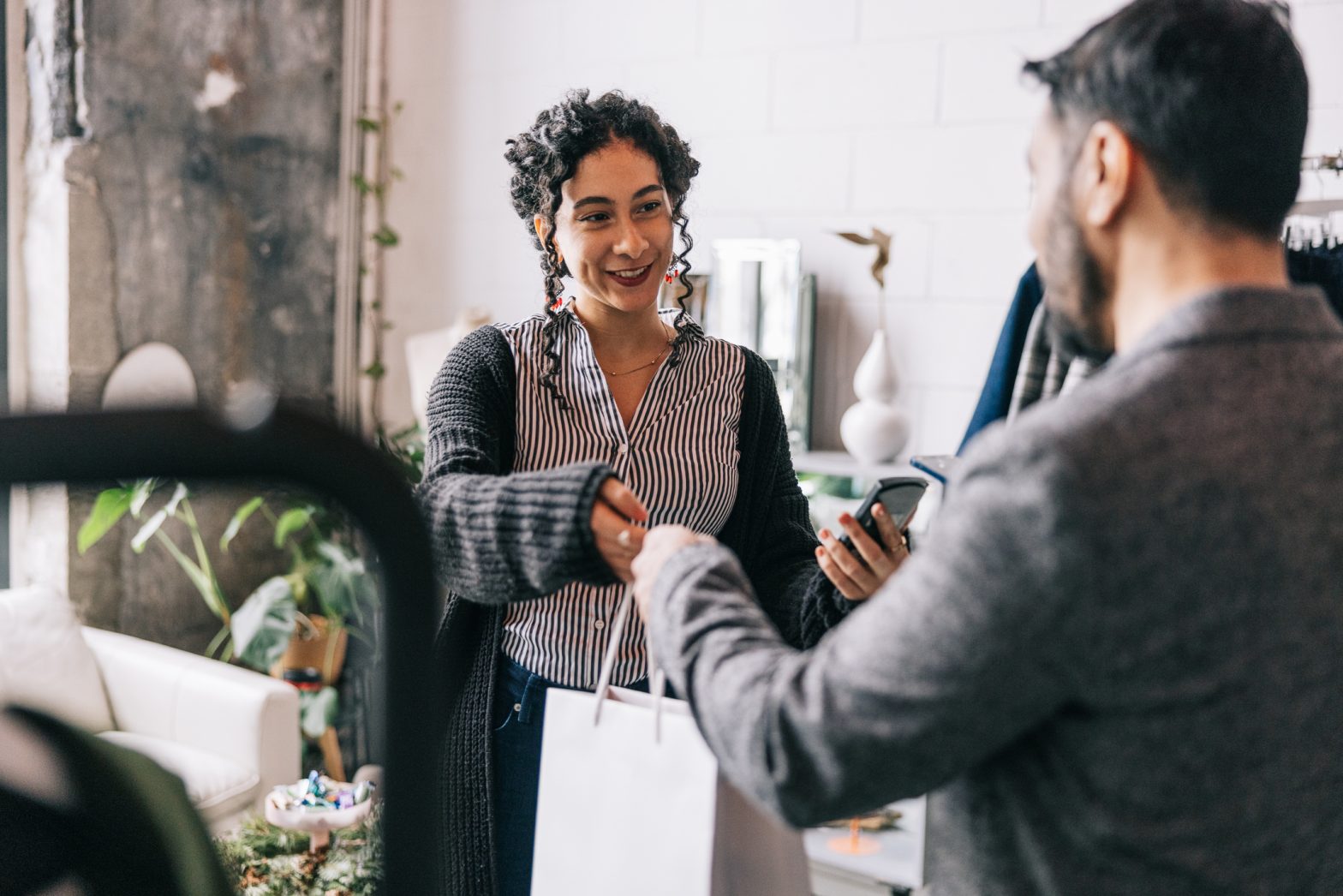 Indian man, dressed in formal attire, makes a mobile payment for his purchase at a clothing store, the use of technology making his shopping experience seamless.