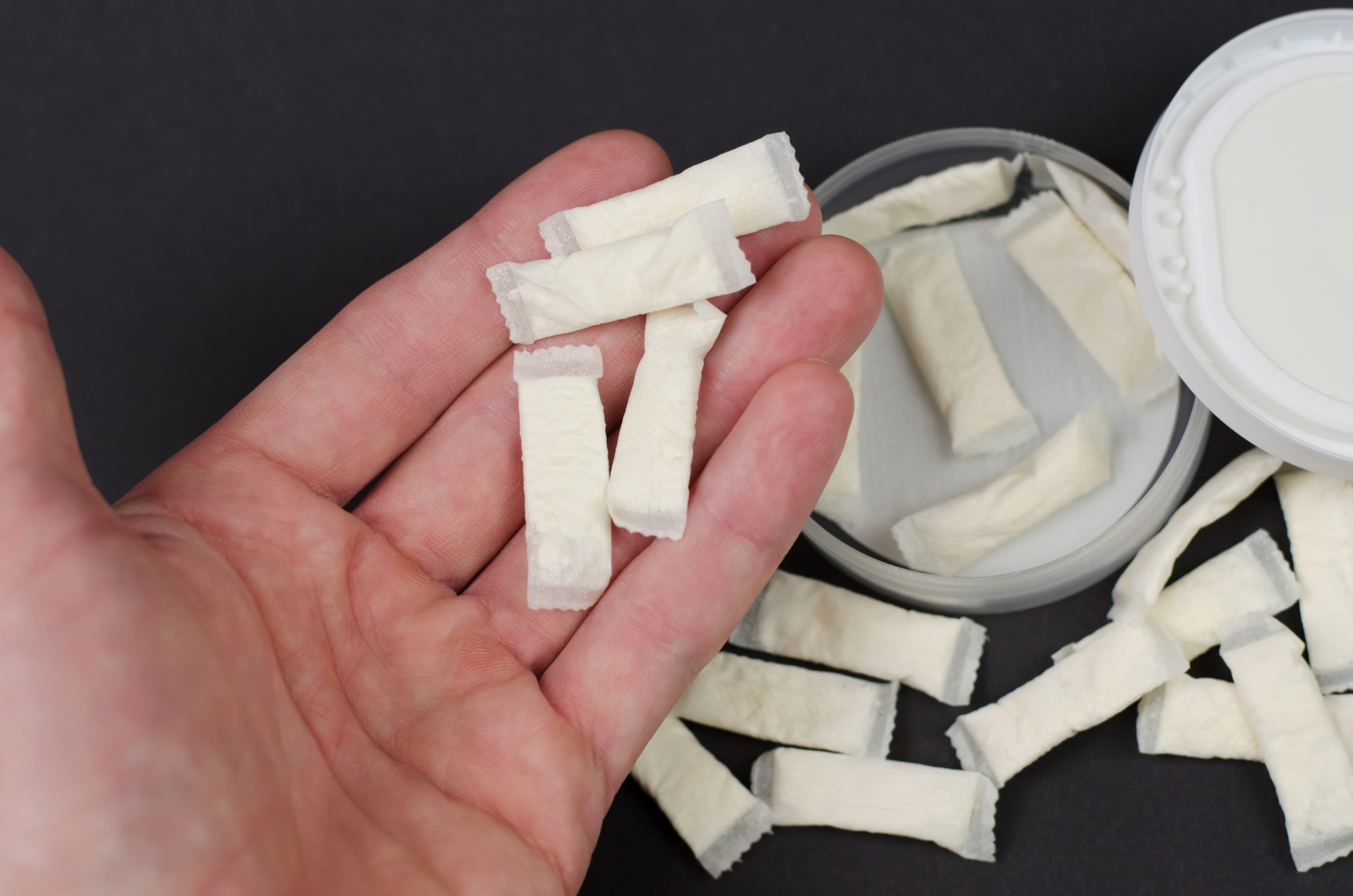Hand holding nicotine pouches against a black background.