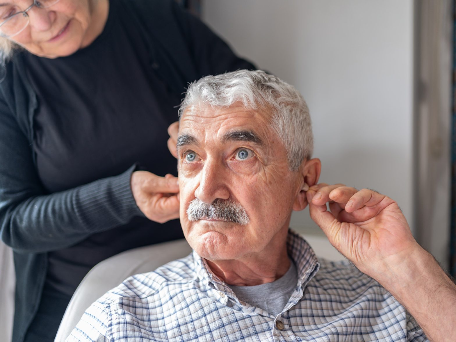 Senior Woman Helping Her Husband With Hearing Aid.