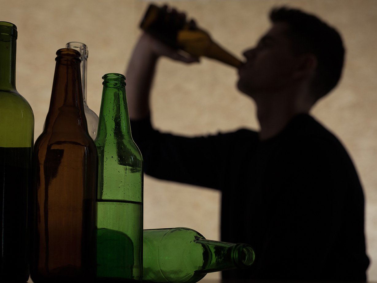A silhouette of a person drinking from a bottle, with various bottles in the foreground.
