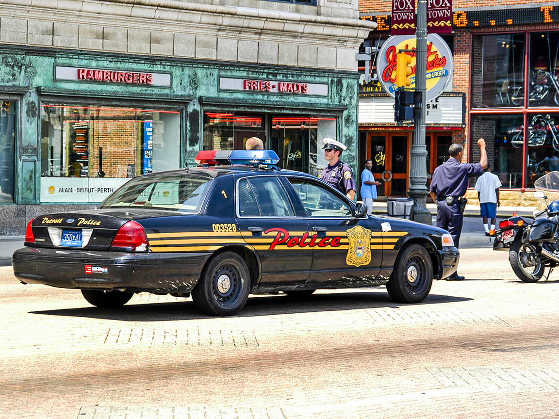Detroit Police car parked on a city street with two officers nearby.
