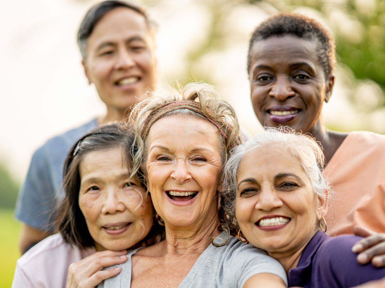 Diverse group of senior friends smiling together outdoors in a park setting.
