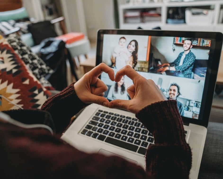 Image of hands forming a heart shape in front of a laptop that displays a group video call