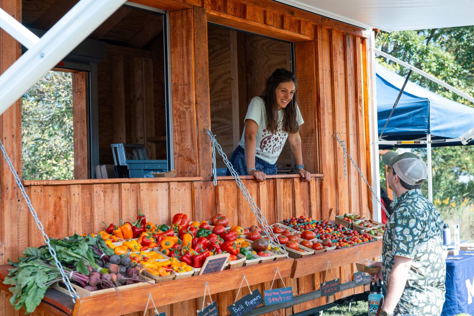 A student leans out of the window of the mobile farm stand over the shelves of fresh produce to talk to a customer at the Campus Farm during Harvest Fest.