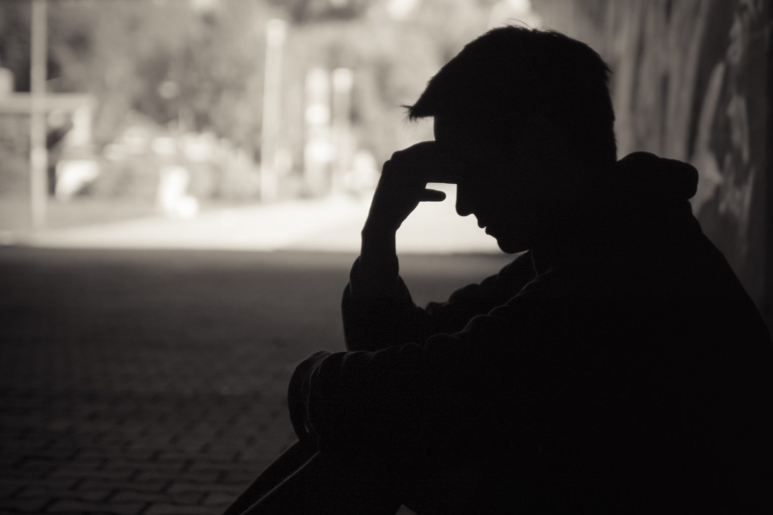 Young emotional man in need of help sitting in a sad dark street setting