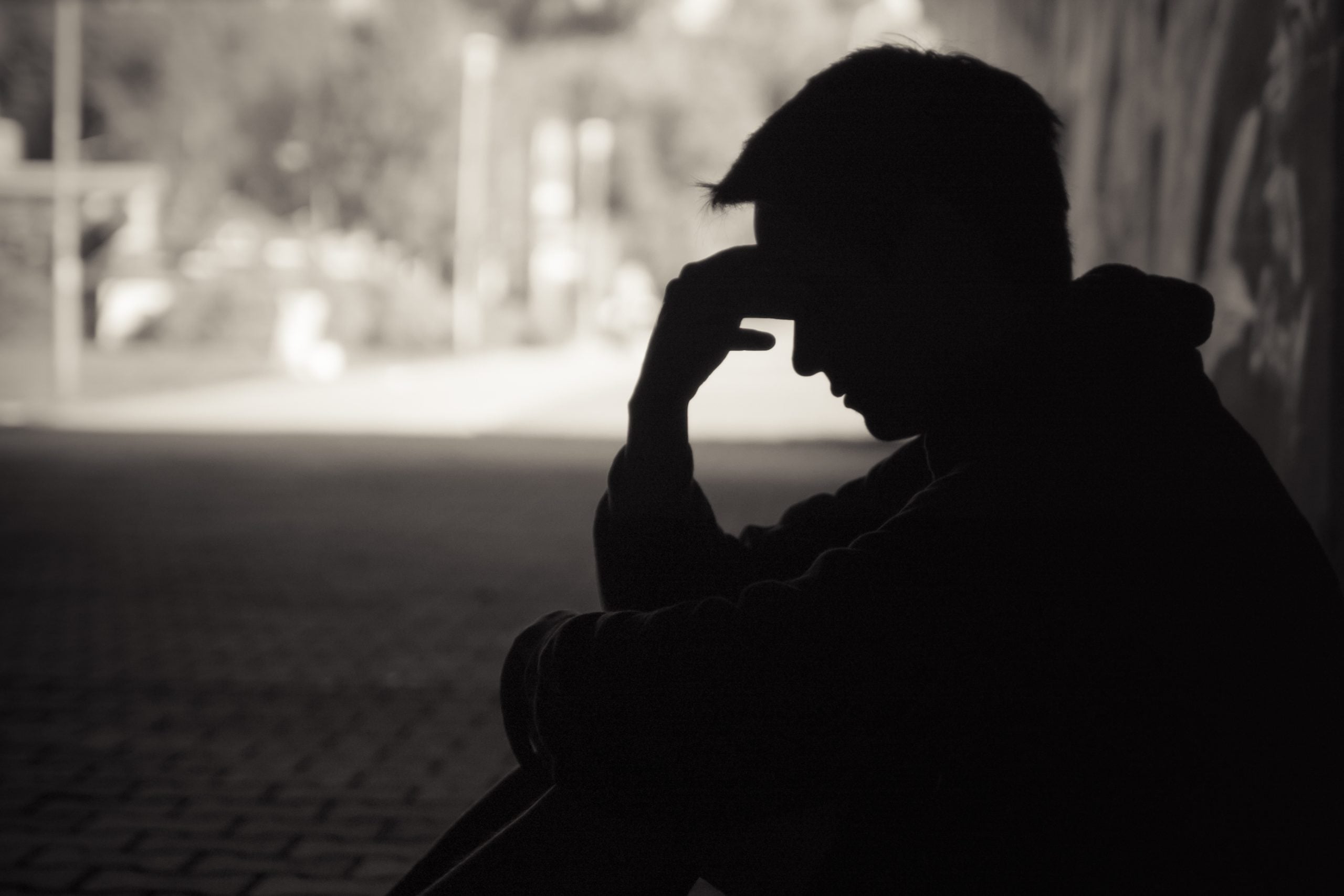 Young emotional man in need of help sitting in a sad dark street setting