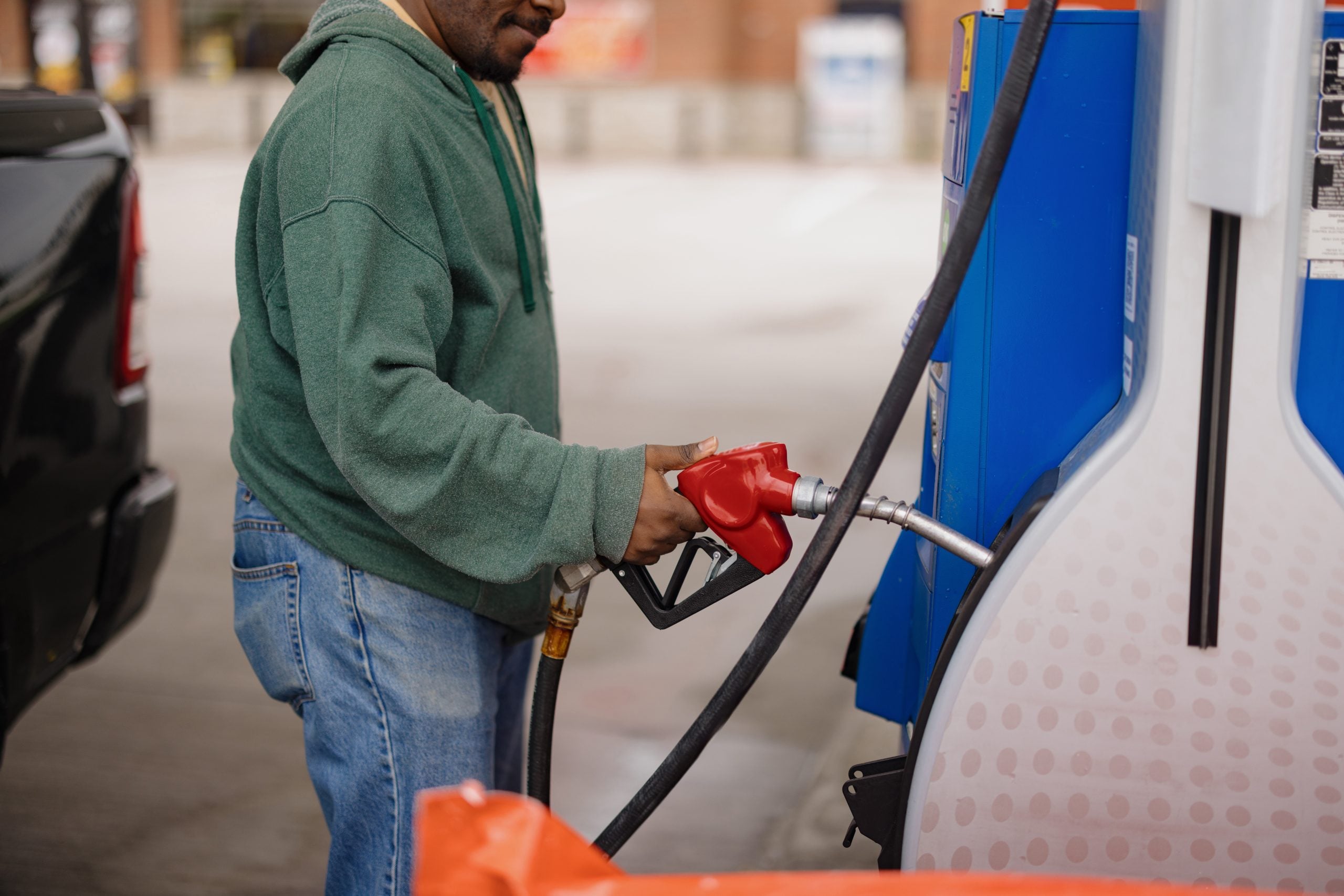 Man holding a red gas nozzle fueling a car at a gas station, providing essential energy for transportation