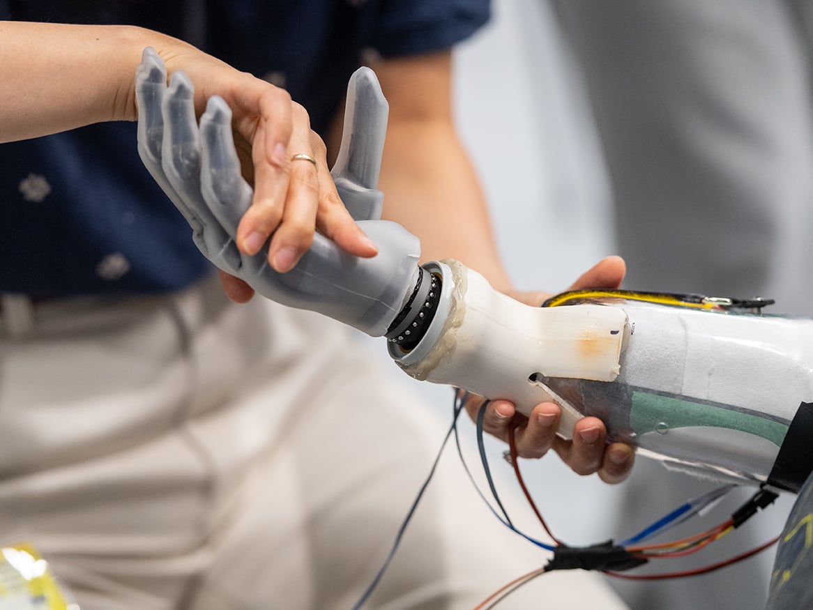 A Kinesiology Research student tests the grip of a prosthetic robot hand with a study participant.