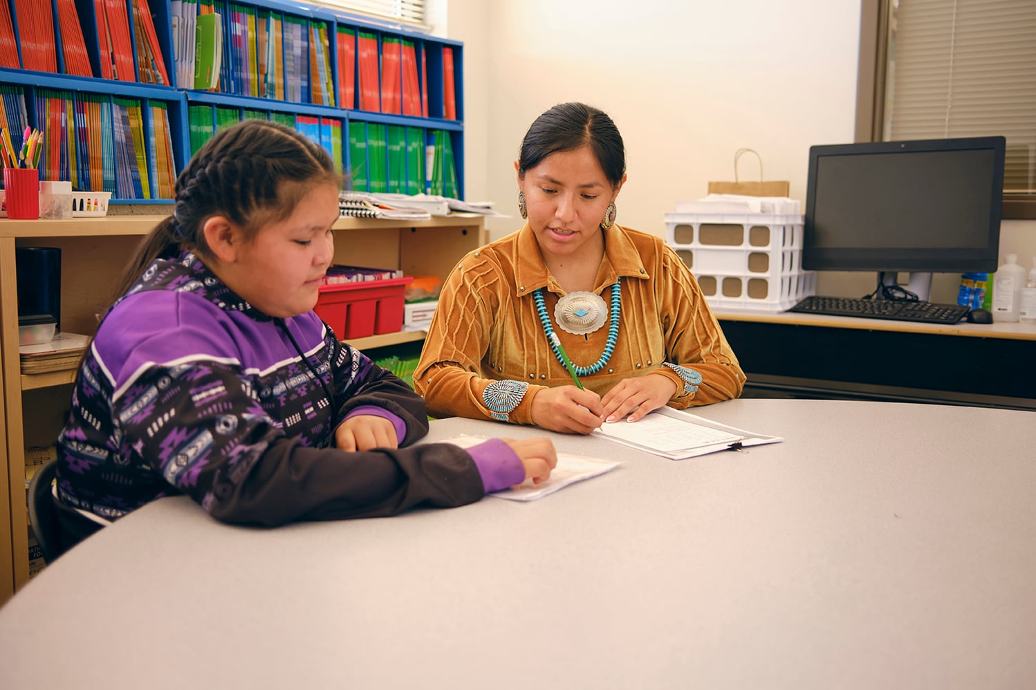 A Native American Navajo elementary age student in a school classroom working with a teacher individually.