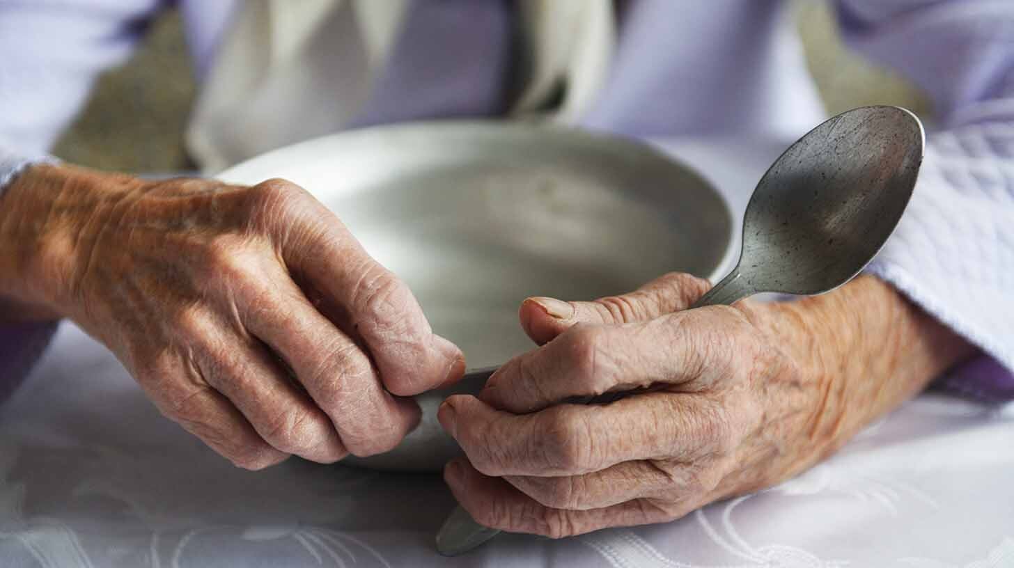 elderly hands holding an empty aluminum bowl and spoon. credit: Adobe Stock.